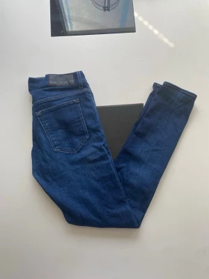 Mörkblå slim fit jeans - Snygga mörkblå slim fit jeans med klassisk femficksdesign och läderpatch i midjan. Jeansen har en smal passform och är tillverkade i stretchigt denimtyg för extra komfort. Perfekta för en trendig och avslappnad look.