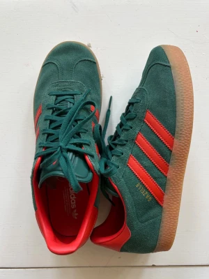 Adidas Originals Gazelle, gröna och oranga sneakers - Adidas Gazelle sneakers i grön mocka med oranga detaljer. Ascoola och trendiga. Endast använda 1 gång. Nypris, 1249kr.