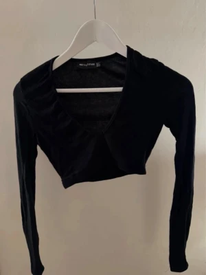 Svart croppad topp PrettyLittleThing - Snygg svart croppad bolerotopp från PrettyLittleThing med v-ringning och långa ärmar. 