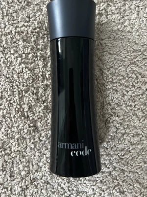 Armani Code Eau de Toilette 75ml - Säljer en elegant parfymflaska från Armani Code, Eau de Toilette. Flaskan är svart med en stilren, böjd form och har en matt mörkgrå kork. Volymen är 75 ml och flaskan är tillverkad i glas. Perfekt för dig som gillar exklusiva dofter. Cirka hälften kvar 