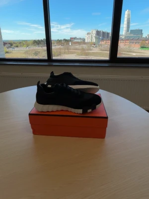 Svarta sneakers med vit sula - Säljer ett par stilrena svarta sneakers med chunky vit sula och svarta detaljer undertill. Skorna har en låg profil och är tillverkade i textilmaterial med snörning. Perfekta för dig som gillar en modern och sportig look.