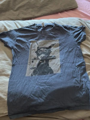 Blå t-shirt med hundtryck - Cool blå t-shirt med tryck av en hund på framsidan. T-shirten har rund hals och korta ärmar, perfekt för en avslappnad stil. Materialet känns mjukt och bekvämt, troligtvis bomull. Passar dig som gillar unika motiv och streetwear.