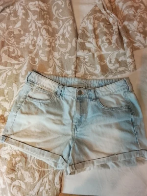 Ljusblå denimshorts från H&M nyskick  - Snygga ljusblå denimshorts från H&M med klassisk femficksdesign och uppvikta benslut. Shortsen har bälteshällor och knappgylf, perfekta för varma dagar. Stilsäkert val till sommargarderoben! Nyskick 