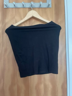 Kort svart tajt kjol - En svart bandeau tubtopp i mjukt och stretchigt material. Toppen är axelbandslös och har en tight passform som sitter snyggt på kroppen. Enkel och stilren design utan synliga detaljer eller mönster. Står ingen storlek men skulle säga S