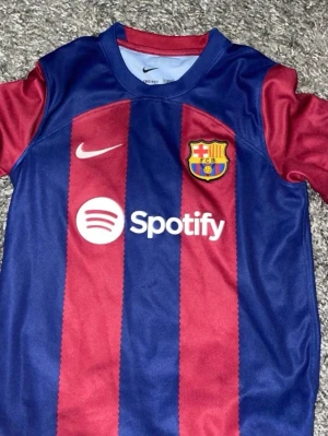 FC Barcelona matchtröja Nike - Säljer en FC Barcelona matchtröja från Nike med klassiska blå och vinröda ränder. Tröjan har klubbmärket, Nike-logga och Spotify som sponsor framtill. Perfekt för dig som älskar fotboll och vill visa ditt stöd för Barca.köpt I riktiga Barcelona shoppen för 1200
