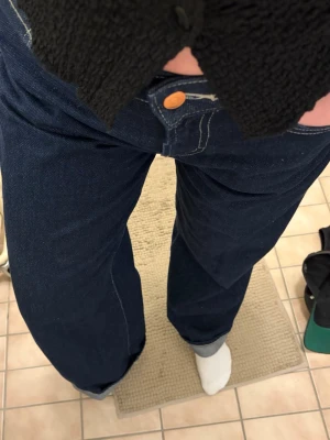 Mörkblå raka jeans med kontrastsömmar - Säljer ett par mörkblå jeans med raka ben och tydliga kontrastsömmar. Klassisk femficksmodell med gylf och knapp i kopparfärg. Jeansen har en tidlös look och är tillverkade i kraftigt denimtyg.