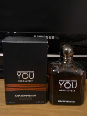 Emporio Armani Stronger With You - Emporio Armani Stronger With You Absolutely är en elegant herrparfym i en mörkbrun glasflaska med silverfärgad kork. Flaskan har en stilren, fyrkantig form och kommer med originalkartong i svart med kopparfärgade detaljer. Doften är intensiv och modern. Ca 80-85 ml kvar om inte mer
