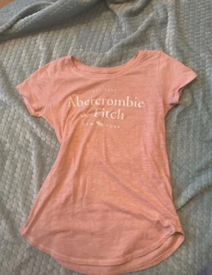 Coral Abercrombie & Fitch t-shirt - Säljer en coral t-shirt från Abercrombie & Fitch med vit logotyptryck på bröstet. T-shirten har rund hals och korta ärmar, perfekt för en avslappnad och cool look. Materialet är mjukt och känns skönt mot huden. Skriv vid frågor, pris kan diskuteras💕