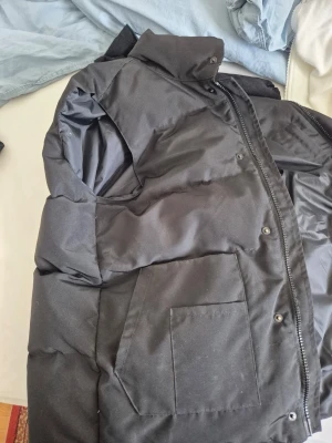 Svart dunjacka från Canada Goose - Säljer en svart dunjacka från Canada Goose med hög krage och dragkedja framtill. Jackan har stora fickor på utsidan och meshficka på insidan. Klassisk puffer-modell som håller dig varm under kalla dagar. Passar perfekt för vintern och du kan också ha den för sommaren den är xl men också passar som L priset kan diskuteras 