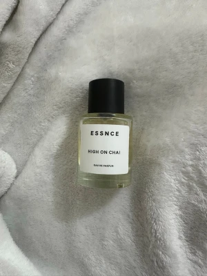 ESSNCE High On Chai Eau de Parfum - Parfymflaska från ESSNCE med doften High On Chai. Flaskan är cylindrisk i genomskinligt glas med svart lock och vit etikett med svart text. Modern och stilren design, perfekt för dig som gillar unika dofter.