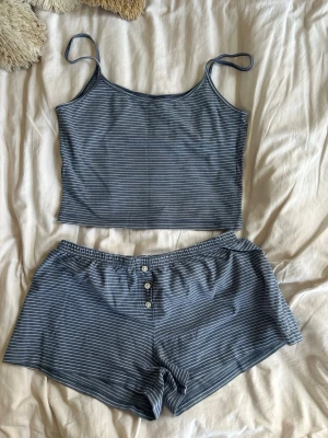 Brandy pyjamas - Mysigt pyjamas-set i blått med tunna vita ränder. Setet består av ett linne med smala axelband och matchande shorts med knappar framtill och resår i midjan. Perfekt för chillkvällar hemma. Onesize men passar som S