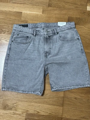 Grå denimshorts från Zara - Snygga grå denimshorts från Zara med klassisk femficksdesign och normal passform. Shortsen har bälteshällor och stängs med knapp och dragkedja. Perfekta för en avslappnad stil under varmare dagar. Helt oanvända 