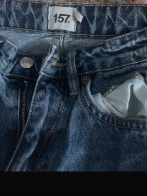 Blå raka jeans från 157 - Säljer ett par klassiska blå jeans från 157 med raka ben och hög midja. Jeansen har dragkedja, knapp och fem fickor. Perfekta för en avslappnad och trendig look. Tillverkade i slitstark denim.
