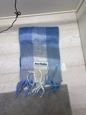 Blå och vit rutig halsduk Acne Studios - Supermjuk halsduk från Acne Studios i rutigt mönster med olika nyanser av blått och vitt. Gjord i fluffig mohairblandning och har långa fransar i ändarna. Perfekt för att ge din outfit en cool touch.
