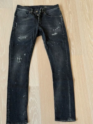 Svarta skinny jeans med slitningar från Dondup strl 30 - Snygga svarta skinny jeans med slitningar och distressed detaljer samt stänk för en cool, trendig look. Klassisk femficksmodell med knappgylf. Perfekta för dig som gillar streetstyle och vill sticka ut.