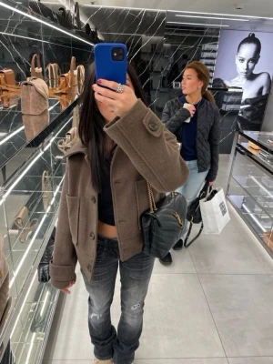 Kort brun ulljacka med stora fickor - Säljer en kort, boxig brun jacka med stora knappar och två rejäla fickor framtill. Jackan har en bred krage och är tillverkad i ett tjockt ullmaterial som ger en stilren och trendig look. Perfekt för dig som gillar en avslappnad men snygg stil.