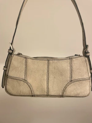 Beige axelväska från Zara - Snygg beige axelväska i mockaimitation med markerade sömmar och axelband med spänne i silverfärg. Väldigt unik stil. 