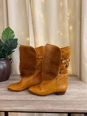 Vintage äkta läder & päls boots  - Unika bruna boots i läder med mjuk pälsdetalj framtill och dekorativ snörning på sidan. Bootsens spetsiga tå och låga klack ger en cool vintagekänsla. Perfekta för dig som vill sticka ut med din stil och gillar naturmaterial och detaljer.