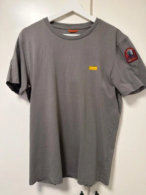 Grön t-shirt från Parajumpers - Snygg grön t-shirt från Parajumpers med korta ärmar och rund hals. Liten gul logotyp framtill och ett coolt märke på ena ärmen. Perfekt för en avslappnad och stilren look.