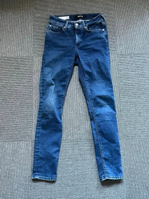 Blå skinny jeans från Replay - Säljer ett par klassiska blå skinny jeans från Replay med fem fickor och snygga kontrastsömmar. Jeansen har normal midja och är tillverkade i stretchigt denim för en bekväm passform. Perfekta till en avslappnad stil.