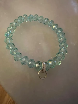 Thomas sabo, Turkost pärlarmband med ringdetalj - Säljer ett snyggt armband med turkosa, facetterade pärlor som ger ett glittrande intryck. Armbandet har en silverfärgad ringdetalj thomas sabo. . Perfekt för dig som gillar unika accessoarer med lite extra bling. Du kan hänga berlocker på ögglan