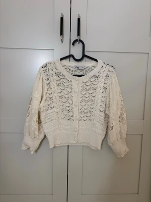 Vit spetskofta från Zara - Superfin vit kofta från Zara med spetsdetaljer och mönsterstickning. Koftan har rund halsringning, knappar framtill och puffiga trekvarts ärmar med broderade detaljer. 