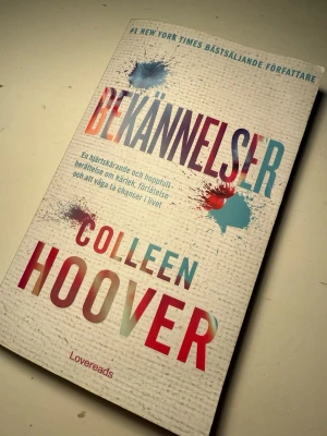 Bekännelser av Colleen Hoover - En gripande roman av Colleen Hoover med färgstarkt omslag och stänk av blått och rött. Boken handlar om kärlek, förlåtelse och att våga ta chanser i livet. Perfekt för dig som gillar känslosamma berättelser. På svenska! 