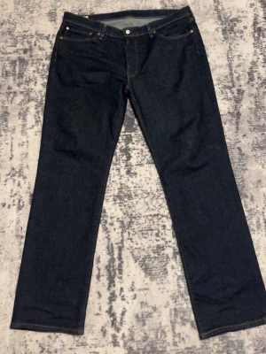 Mörkblå raka jeans från Levi's - Snygga mörkblå jeans från Levi's med klassisk rak passform. Jeansen har fem fickor, gylf med knapp och dragkedja samt kontrastsömmar. Tillverkade i slitstark denim med en tidlös look.  Storlek W38 L32 är 1.86 m, så rekommenderar till någon som är över 1.88 m 