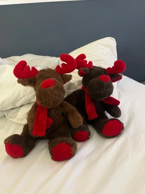 Två mjuka ren-gosedjur med röda detaljer - Säljer två söta ren-gosedjur i mjuk plysch, en ljusbrun och en mörkbrun. Båda har röda horn, nos, halsduk och tassar. Perfekta som juldekoration eller present. Klassisk rund form och mysigt material. 