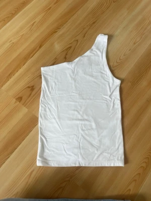 Vit oneshoulder topp från Gina Tricot - Snygg vit oneshoulder topp från Gina Tricot i mjuk bomull. Enkel och stilren design med en axel och tight passform. Perfekt att matcha med jeans eller kjol för en trendig look.