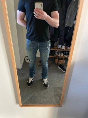 Tiger Of Sweden Leon - Säljer ett par blå slim fit jeans med slitningar och lätt tvättad look. Jeansen har klassisk femficksdesign och läderpatch bak i midjan. Perfekta för en avslappnad och trendig stil. Storleken är 30/32