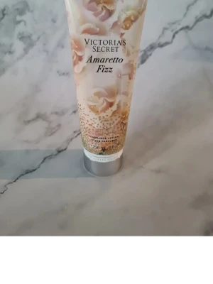 Victoria's Secret Amaretto Fizz lotion - Fräsch doftande bodylotion från Victoria's Secret i varianten Amaretto Fizz. Tuben är dekorerad med blommor och guldiga detaljer. Innehåller 236 ml och har noter av mandelkaffe och apelsinblomma. Perfekt för dig som vill ha en lyxig och väldoftande hudvård. Helt ny och oanvänd 