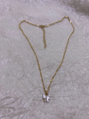 Guldhalsband med pärlemorfjäril - Snyggt halsband i guldton med en vriden kedja och ett hänge i form av en fjäril i pärlemor. Perfekt accessoar för att lyfta din outfit med en unik detalj. Justerbar längd för bästa passform.