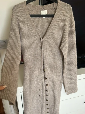 Beige långklänning  - Säljer en beige ribbad långklänning med v-ringning och långa ärmar. Klänningen har knappar hela vägen framtill och är i ett mjukt stickat material som är super skönt🤍Använd 1 gång
