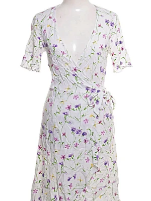 Vit blommig omlottklänning - Söt vit omlottklänning med blommigt mönster i lila, grönt och gult. Klänningen har korta ärmar, v-ringning och knyt i midjan. Perfekt för sommarens alla tillfällen och ger en fräsch och romantisk vibe.