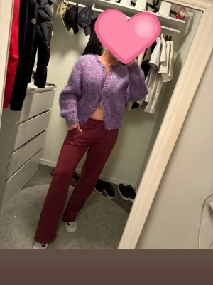 Lila fluffig stickad kofta - Superfin lila stickad kofta med fluffig känsla och diskreta rosa detaljer. Koftan har ballongärmar, knappar framtill och en croppad passform. Perfekt för dig som vill ha en mysig och trendig look. Materialet känns mjukt och gosigt.