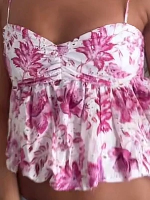 Blommig volang topp med smala band - Söt topp med smala axelband och volangig nederdel. Vit botten med rosa blommigt mönster och lätt rynkad byst. 