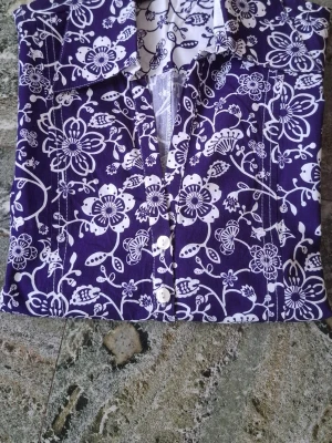 Blommig mörklila skjorta - Snygg långärmad skjorta i mörklila med vitt blommigt mönster. Skjortan har klassisk krage, knappar framtill och är tillverkad i ett mjukt bomullstyg. Perfekt för dig som vill sticka ut med en cool och unik stil. Bystmått: från armhåla till armhåla 50 cm  Studsmått: från sida till sida längst ner 55 cm Längd: uppifrån och ner 60 cm