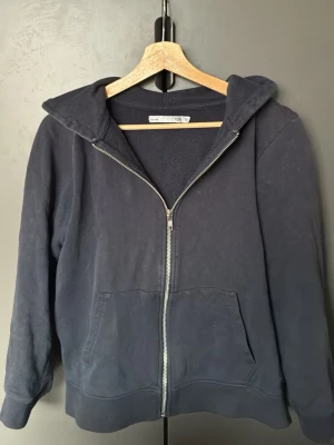 Svart zip hoodie med huva från lager 157 - En enkel och stilren svart hoodie från H&M med dragkedja framtill och två stora fickor. Hoodien har en klassisk huva och ribbade muddar vid ärmar och nederkant. Perfekt för en avslappnad look och passar till det mesta. Plagget kommer från ett rök nikotin och pälsfritt hem, tröjan kommer att tvättas och strykas så att den är ren när den kommer fram till er
