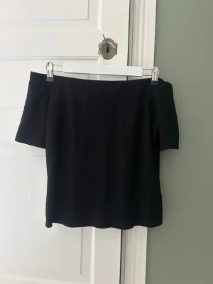 Svart offshoulder topp - En stilren svart offshoulder topp med korta ärmar. Toppen har en enkel och rak passform som ger en clean look. Perfekt att matcha med jeans eller kjol för en trendig outfit. Materialet är typ ett tajt material så inte helt slappt. Har även sytt in lite där uppe vid axlarna då den var lite för bred för mig men det syns absolut inte💕
