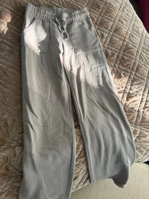 Beiga mjukisbyxor med raka ben - Säljer ett par beiga mjukisbyxor med raka ben och dragsko i midjan. Byxorna har två stora fickor fram och två bakfickor. Tillverkade i mjukt bomullsliknande material, perfekta för chill dagar hemma eller när du vill vara bekväm.