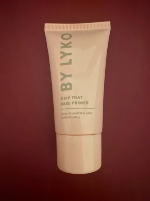By Lyko Grip That Base Primer - Grip That Base Primer från By Lyko i en ljusrosa tub med skruvlock. Primern är framtagen för att ge en jämn och slät bas, och har texten 'skin-plumping and smoothing' på förpackningen. Perfekt för att förbereda huden innan makeup.