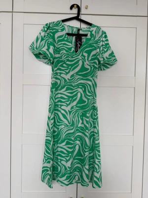 Grön och vit zebramönstrad klänning helt ny  - Säljer grön och vit klänning från Stylein med zebramönster. Klänningen har v-ringning, korta puffärmar. Perfekt för dig som vill sticka ut med ett coolt mönster och sköna vibbar. Helt ny med lappar. 