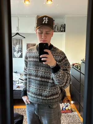 Mönstrad stickad tröja i svart och brunt - En snygg stickad tröja med klassiskt mönster i svart, vitt och brunt. Tröjan har rund hals och ribbade muddar vid ärmslut och nederkant. Perfekt för dig som gillar retrostil och vill ha något varmt och stilrent.