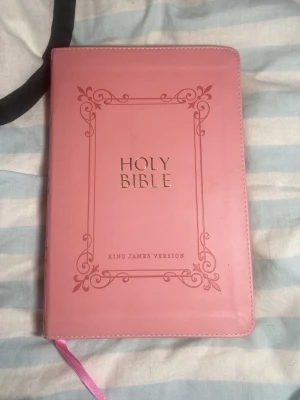 Rosa Holy Bible King James Version - Säljer en snygg rosa Holy Bible i King James Version med gulddetaljer på framsidan och dekorativ ram. Omslaget är i konstläder och boken har ett matchande rosa bokmärke. Perfekt för dig som vill ha en stilren och personlig bibel.