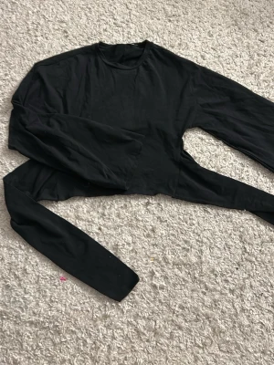 Svart croppad topp med knyt - Hej, jag säljer min svarta tröja med knyt där bak. Den är från lager 157 och inte använd nån gång.