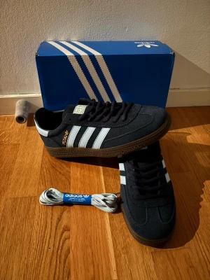 Adidas Spezial blå sneakers - Säljer ett par Adidas Spezial sneakers i blå mocka med vita klassiska stripes och brun gummisula. Skorna har guldfärgad Spezial-text på sidan och kommer med extra skosnören. Perfekta för dig som gillar retrostil och streetwear.