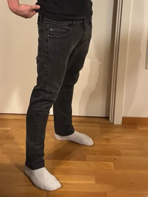 Svarta slim fit jeans från tiger of sweden - Snygga svarta slim fit jeans från tiger of sweden med dragkedjedetalj vid fickan och stora bakfickor. Jeansen har en klassisk femficksdesign och är tillverkade i ett stretchigt denimtyg som sitter skönt. Perfekta för en trendig och avslappnad look.