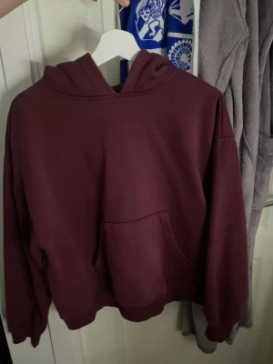 Vinröd hoodie med magficka - Mysig vinröd hoodie från 157 med klassisk huva och stor magficka framtill. Tröjan har en avslappnad passform och ribbade muddar vid ärmslut och nederkant. Perfekt för chill dagar eller när du vill ha något bekvämt och stilrent.