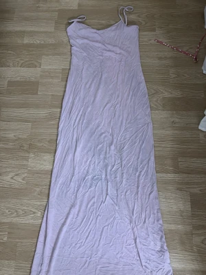 Ljusrosa långklänning med smala band - Säljer en enkel och stilren långklänning i ljusrosa med smala axelband. Klänningen har en rak passform och är ärmlös, perfekt för varma dagar eller sommarens alla tillfällen. Materialet känns mjukt och lätt mot huden.